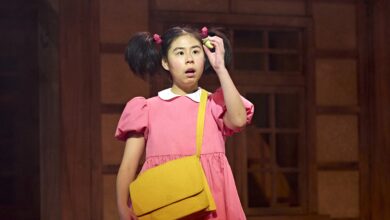 Mei (Victoria Chen) wearing a pink dress and a yellow bag while holding up an acorn.